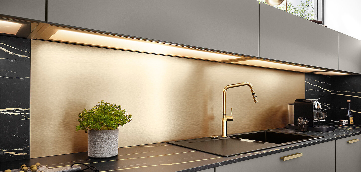 Modern kitchen with sleek black marble countertops, gold accents, under-cabinet lighting, and a potted plant adding a touch of greenery.